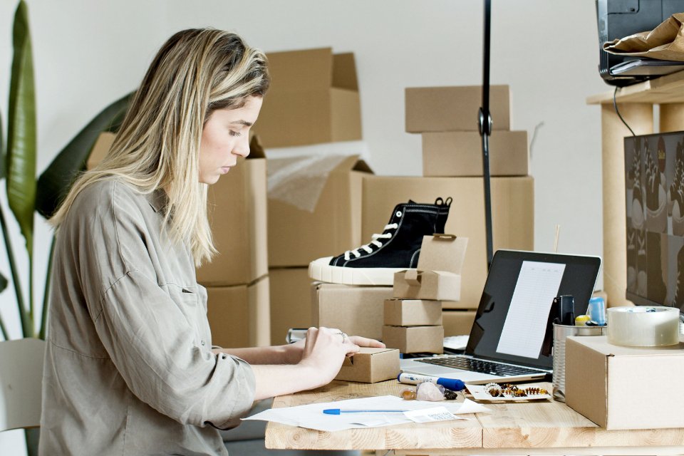 An online retailer preparing product packaging beside a laptop.