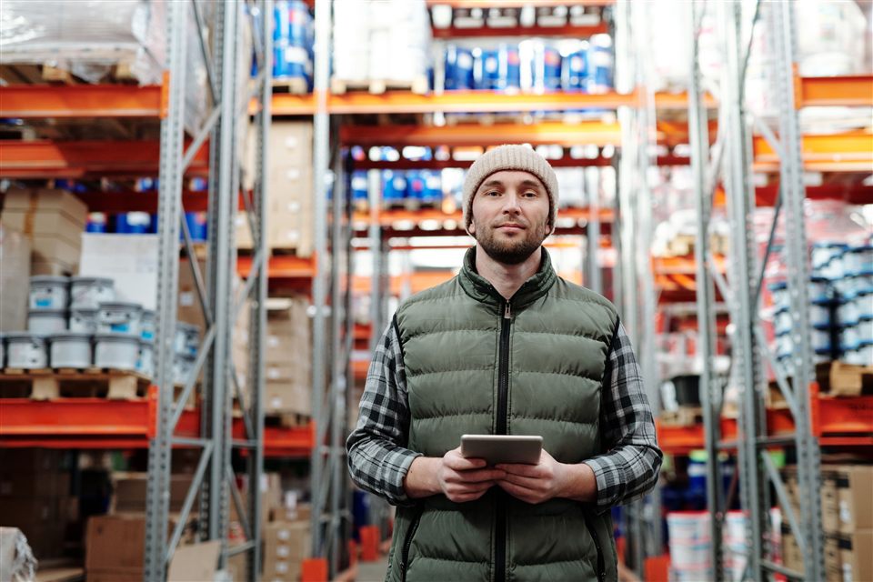 A warehouse worker holding a tablet between inventory shelves.