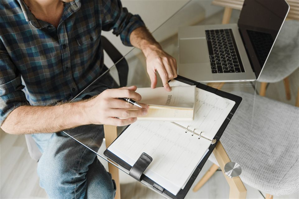 Hands preparing notes in a planner beside a laptop.